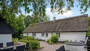A traditional thatched-roof cottage with a paved patio area, furnished with outdoor seating. - 5 Star Holiday Home in Orsted (Ørsted)