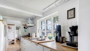 A modern kitchen with white cabinets, a wooden countertop, a coffee machine, and a window providing natural light. - 5 Star Holiday Home in Orsted (Ørsted)