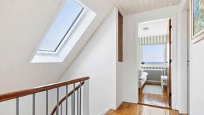 A hallway with wooden flooring, a wooden railing, and a view of a room with a window overlooking a beach. - 4 Star Holiday Home in Allinge (Allinge)