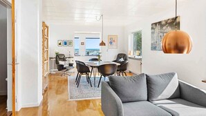 A modern living room with a grey sofa, a dining area with black chairs, and a view of the sea through large windows. - 4 Star Holiday Home in Allinge (Allinge)