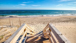 Una pasarela de madera que lleva a una playa de arena, con el océano al fondo.