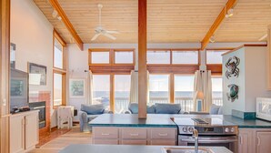 Una cocina amplia con vigas de madera, ventanas grandes, una isla central y vista al océano.