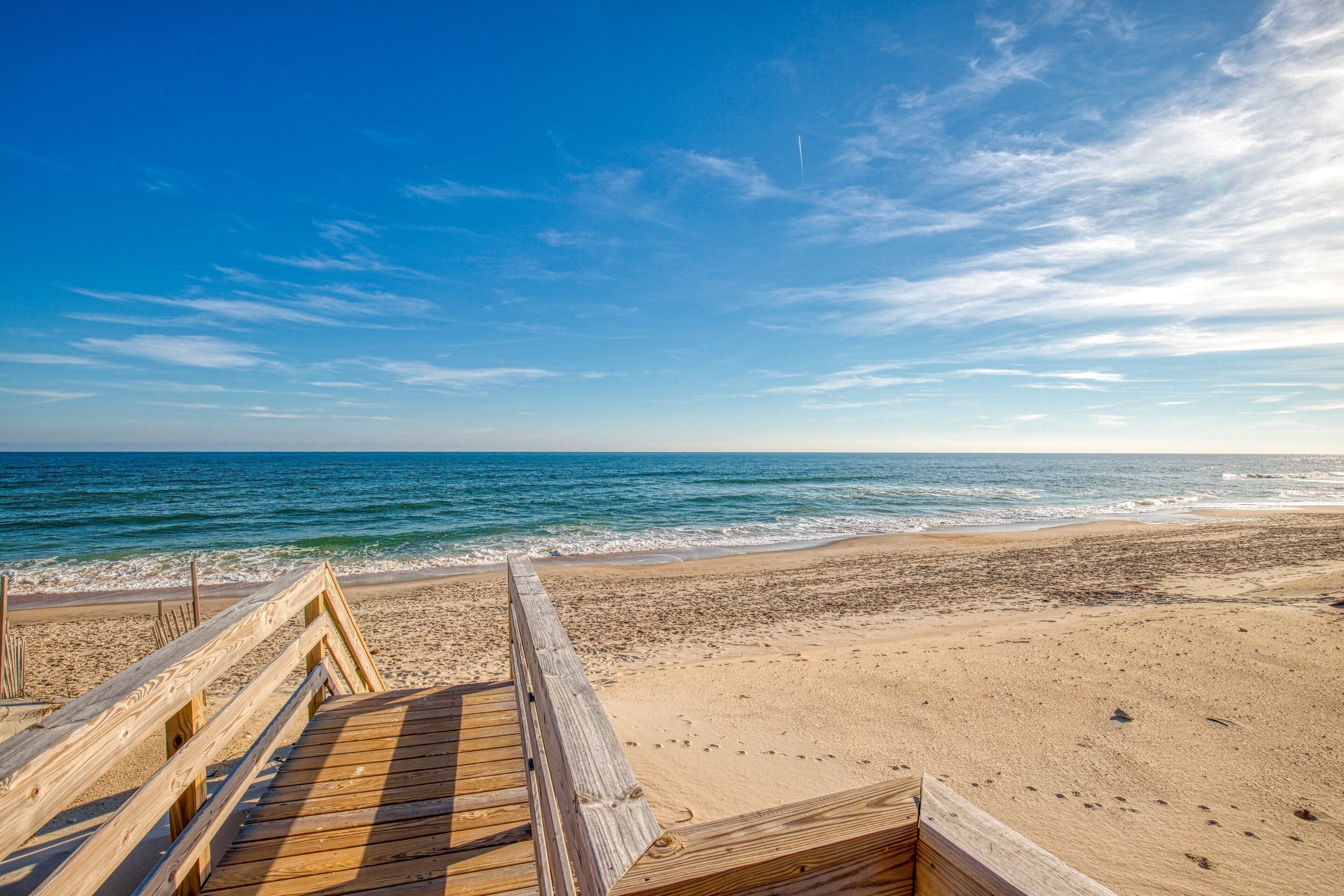 A wooden boardwalk leading to a beach with a clear blue sky and ocean.