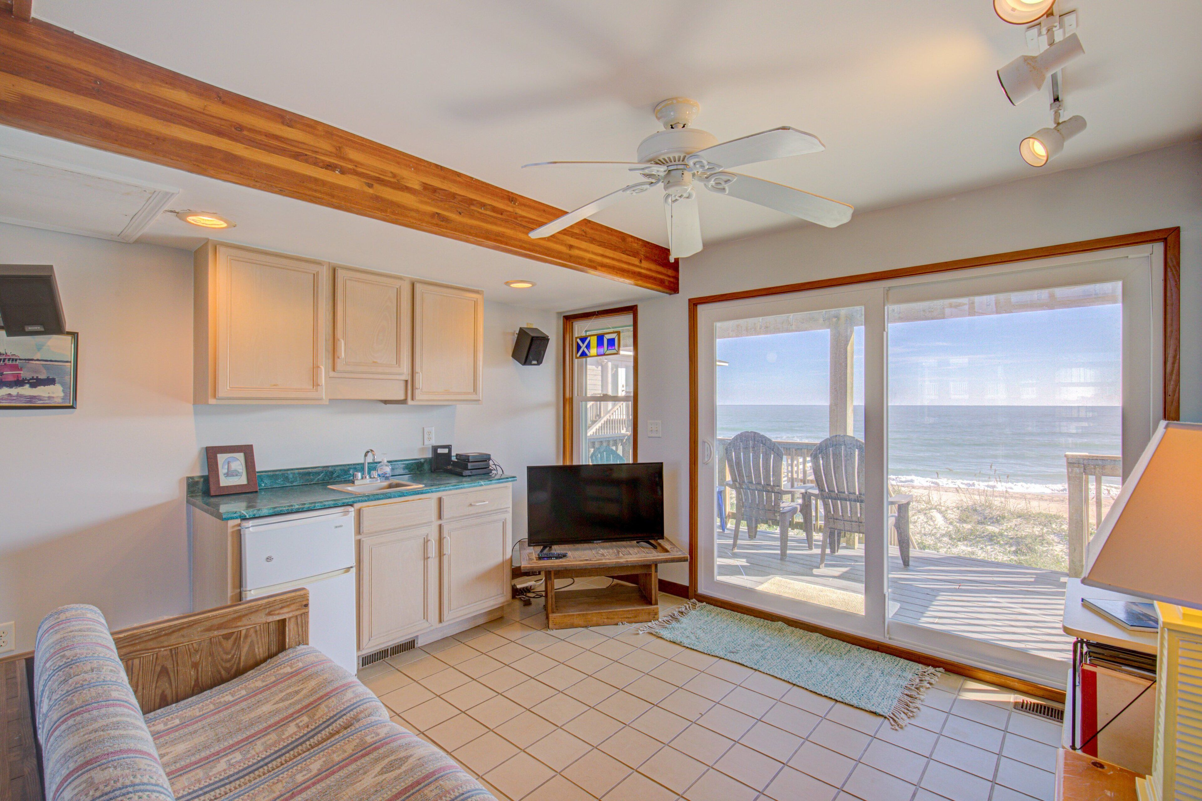 A room with a kitchenette, a television, a sofa, and a view of the beach.