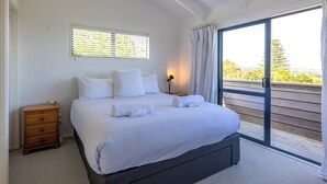 Une chambre avec un grand lit, une table de chevet, une fenêtre avec des stores et une vue sur la verdure.