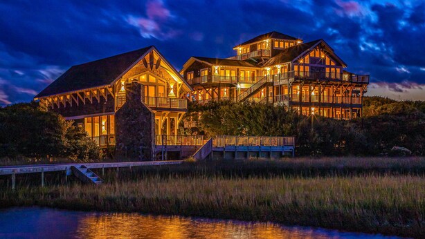 A large, multi-story wooden house with balconies and a dock extending into a body of water. - Luxury sound-front home with private pool, hot tub, & dock (Buxton)