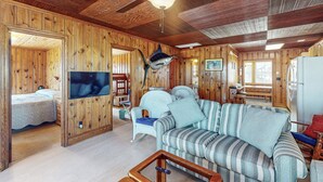 Interior d'una cabana de fusta amb un sofà, una televisió, un ventilador de sostre i una zona menjador.