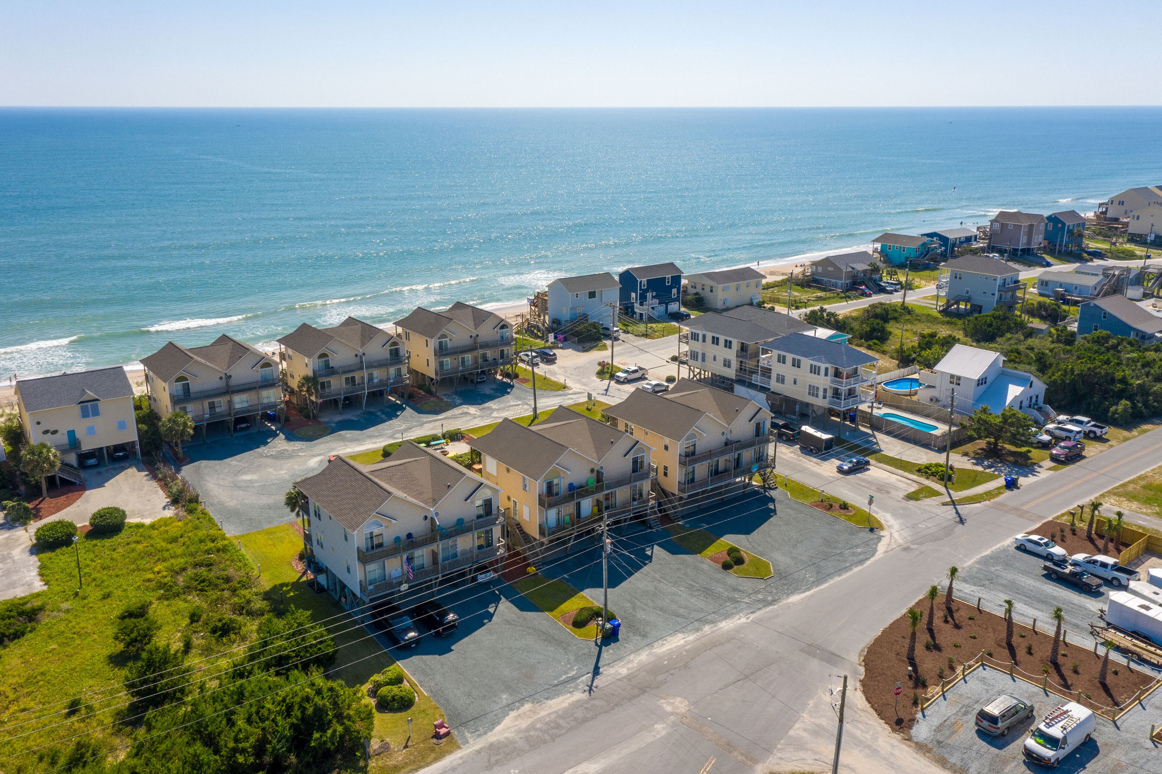 A coastal residential area with houses, a parking lot, and a view of the ocean.