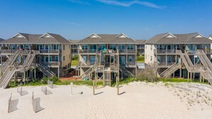 A beachfront hotel with multiple balconies, a sandy beach in front, and a clear blue sky. - Dog-friendly oceanfront home with beach access, a washer/dryer & central AC (Surf City)