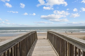 Un muelle de madera que conduce a una playa, con cielo despejado y vista al océano.
