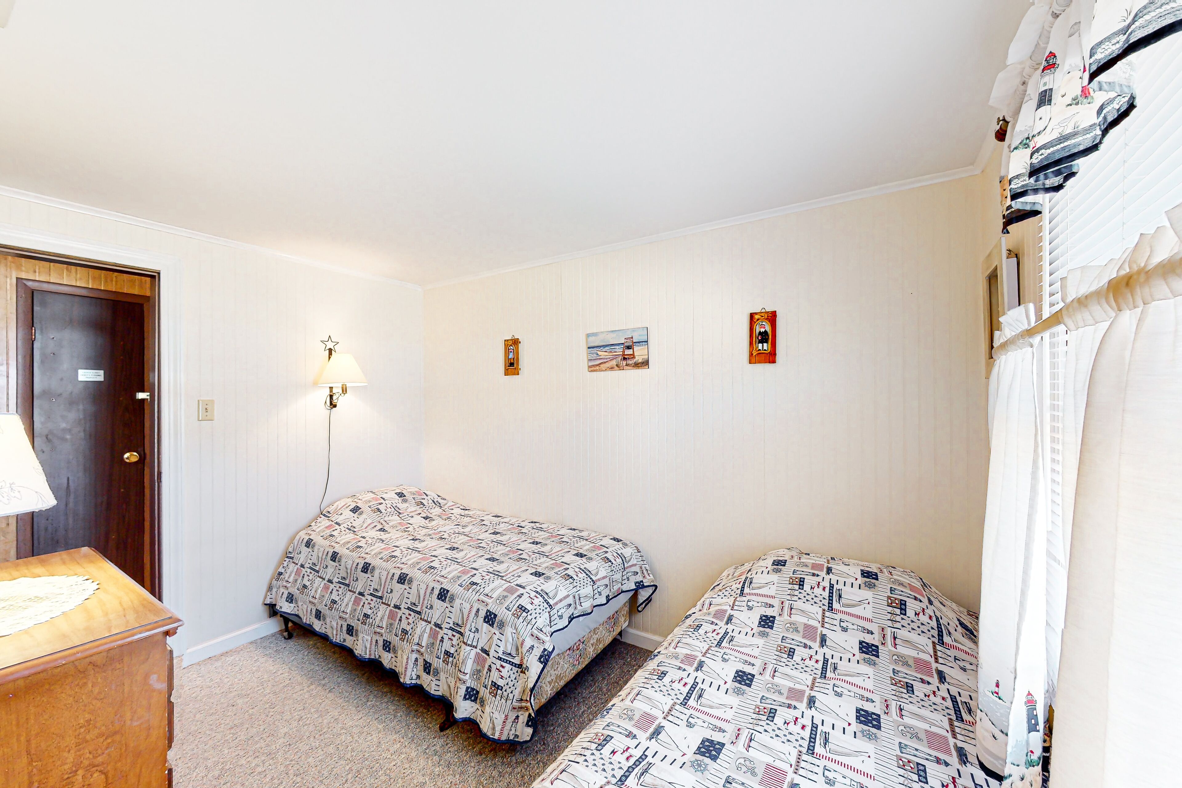 Un dormitorio con dos camas, una mesita de noche de madera, una lámpara de pared y una puerta.