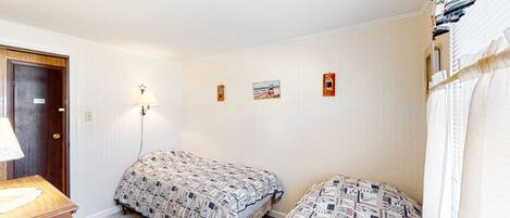 Un dormitorio con dos camas, una mesita de noche de madera, una lámpara de pared y una puerta.