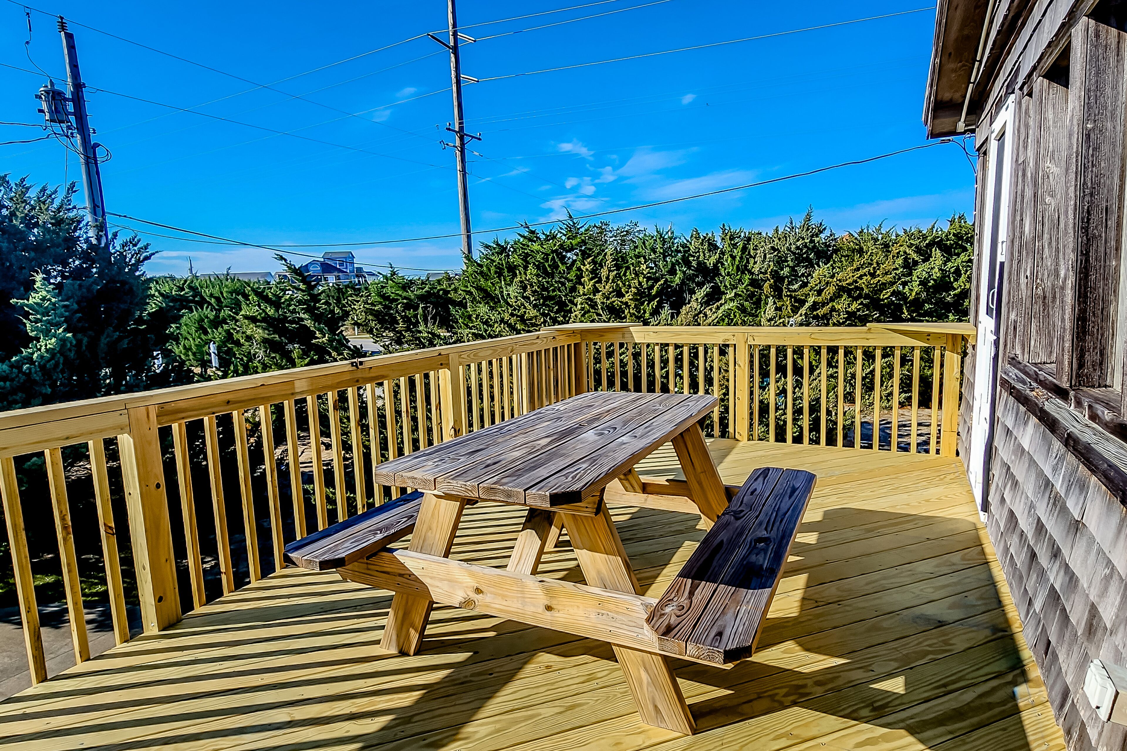 Une terrasse en bois avec une table de pique-nique et des bancs, entourée d’une balustrade en bois.