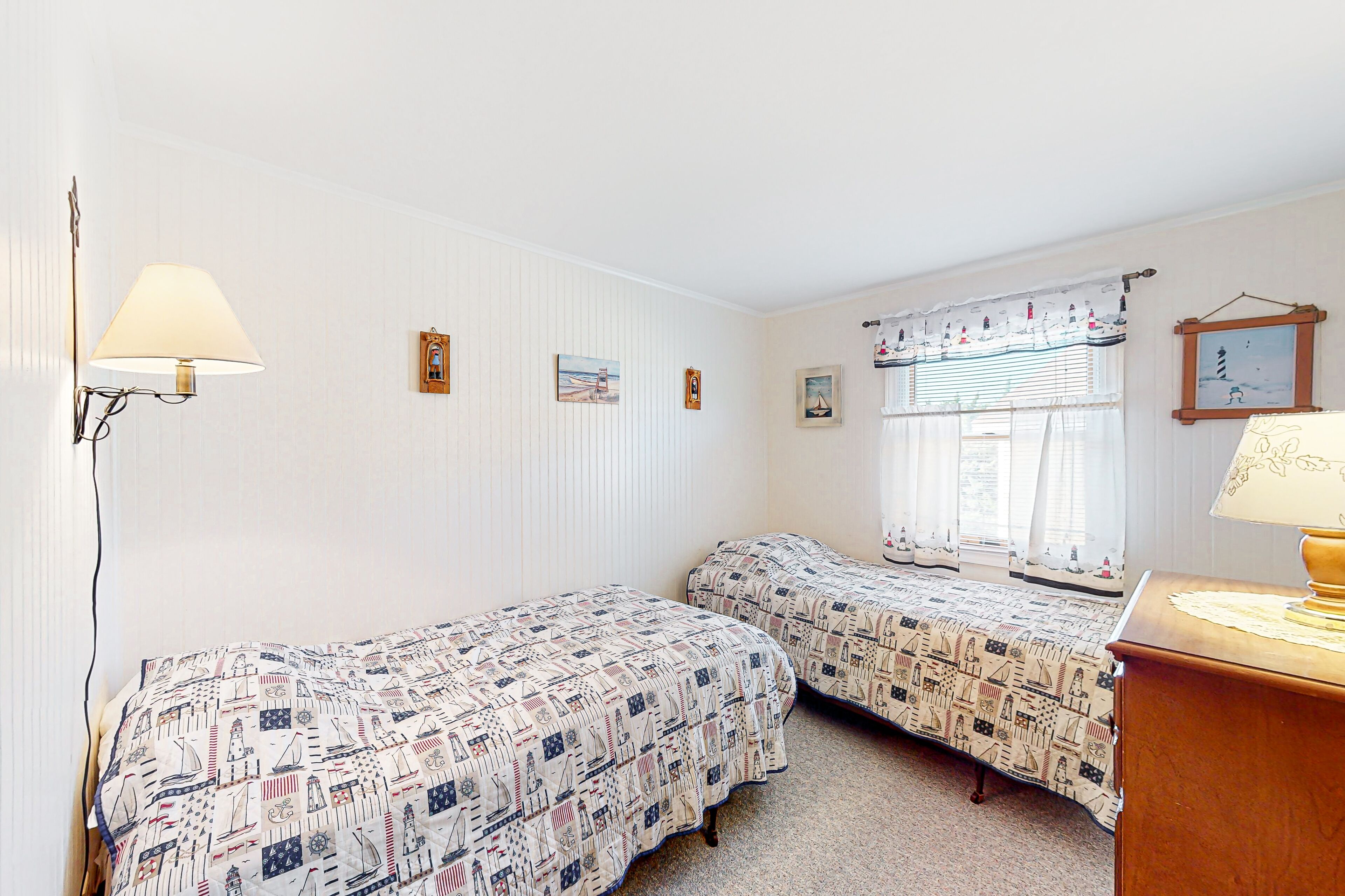 A room with two single beds with nautical-themed bedding, a bedside lamp, and a window with curtains.