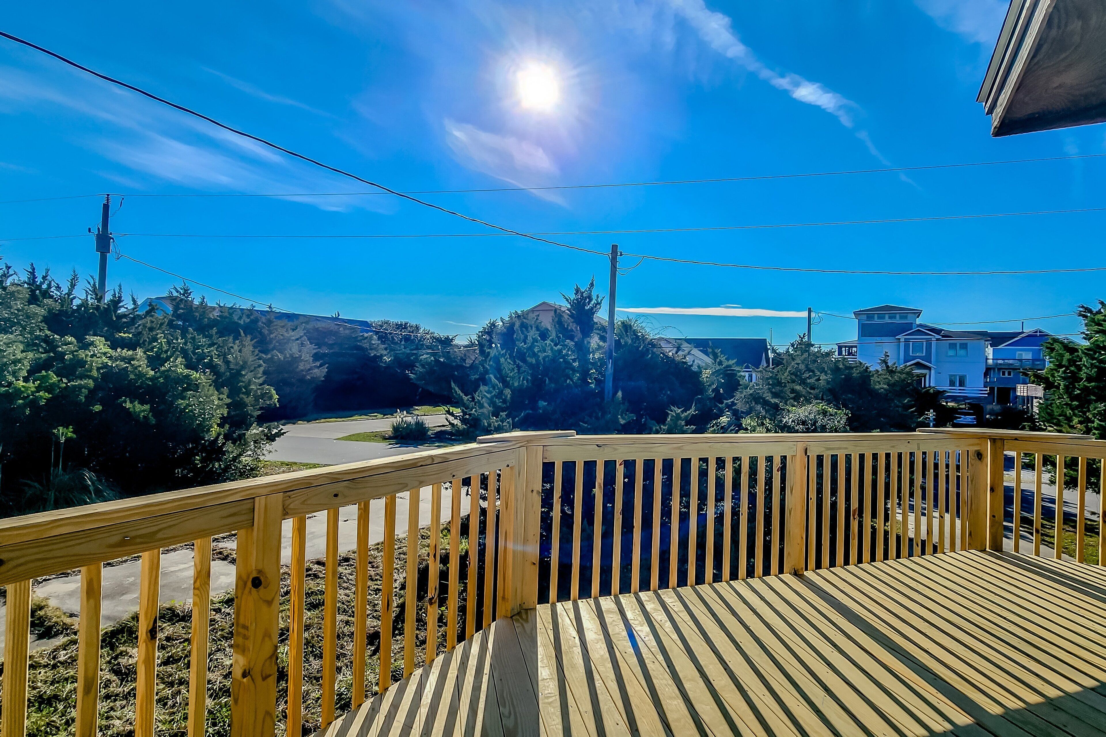 Una terraza de madera con vistas a una carretera, árboles y casas al fondo.
