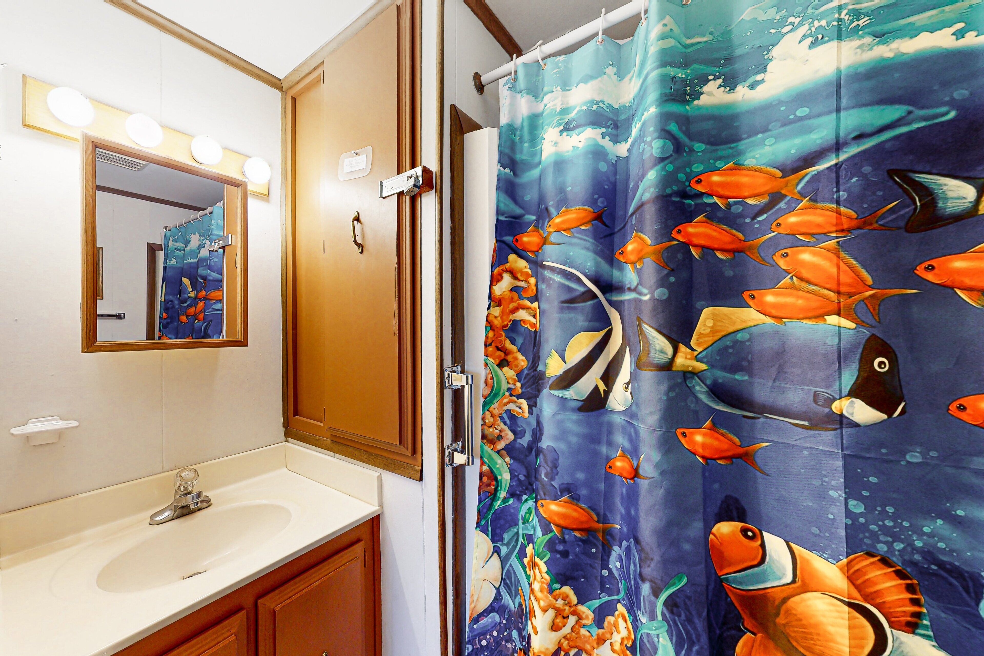 Une salle de bain avec un lavabo, un miroir et un rideau de douche orné de motifs de poissons.