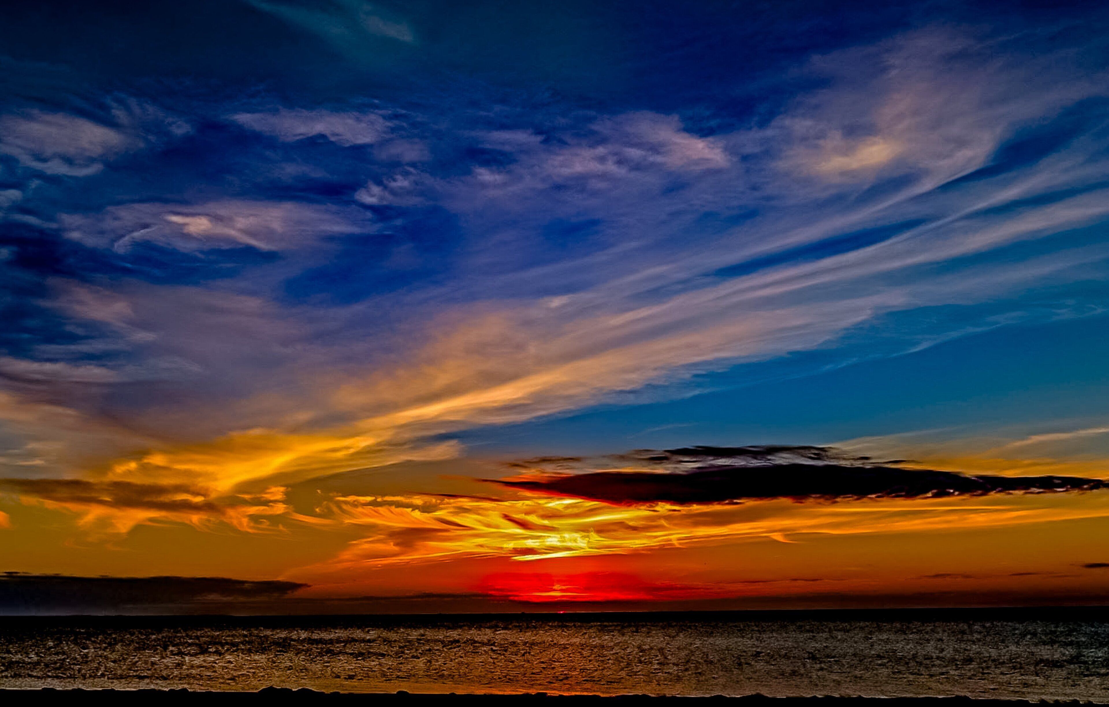 A sunset over a coastal cityscape with a clear sky and visible clouds.