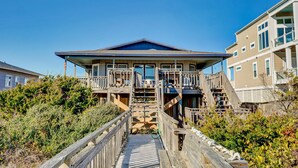 A beachfront house with a wooden deck leading to a balcony, surrounded by dense vegetation. - Oceanfront Home w/Incredible Views, Private Boardwalk to the Beach, & Free WiFi (Holden Beach)