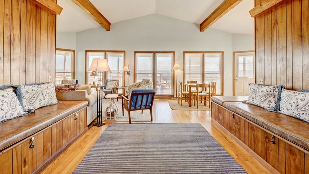 A spacious room with wooden paneling, a large window, a sofa, a chair, and a dining table. - Oceanfront Home w/Incredible Views, Private Boardwalk to the Beach, & Free WiFi (Holden Beach)