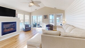 Ein geräumiges Wohnzimmer mit Kamin, Deckenventilator und großem Fenster.