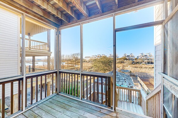 A wooden deck with a glass enclosure, offering views of a residential area and a body of water.