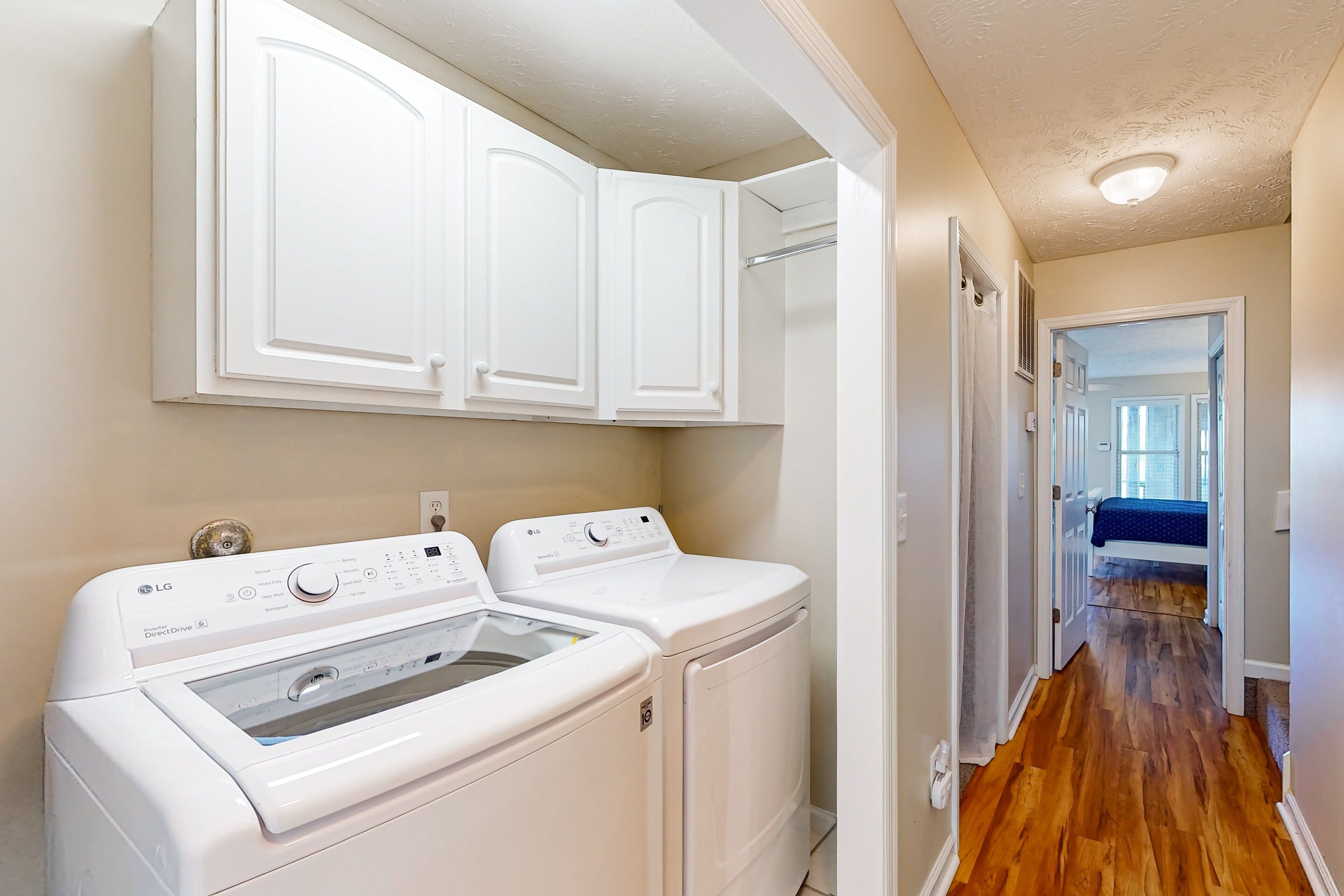 A laundry room with two white front-loading washers and dryers, a white cabinet above, and a wooden floor.