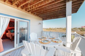A covered outdoor area with a table set for dining, white chairs, and a view of the landscape. - Waterfront condo with pool, central AC, amazing views, & stylish decor (Hatteras)