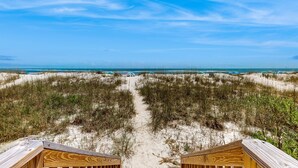 Een strandpad dat leidt naar een houten constructie met uitzicht op de oceaan en duinen.