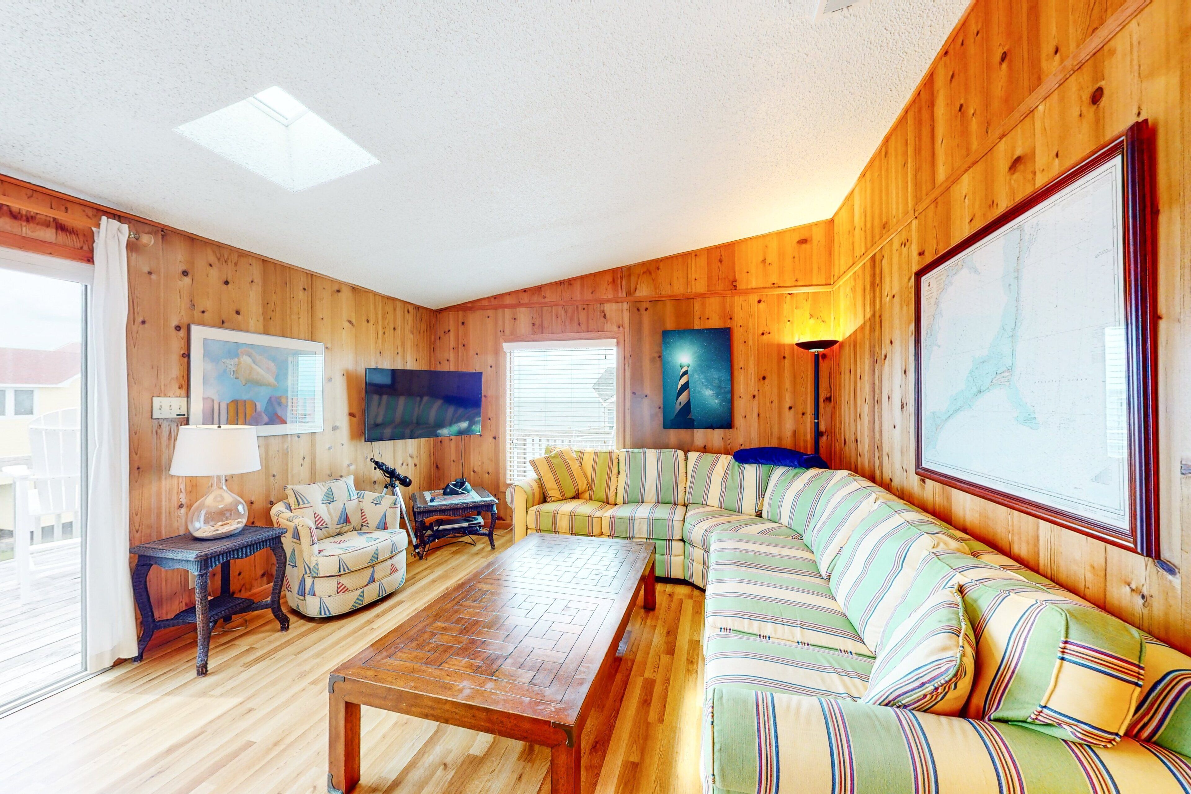 A cozy living room with wooden walls, a striped sofa, a wooden coffee table, and a television.