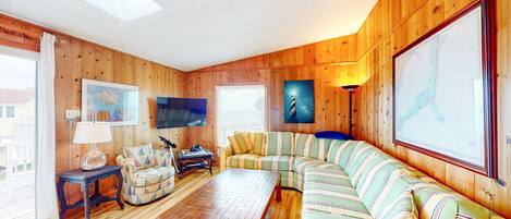 A cozy living room with wooden walls, a striped sofa, a wooden coffee table, and a television.