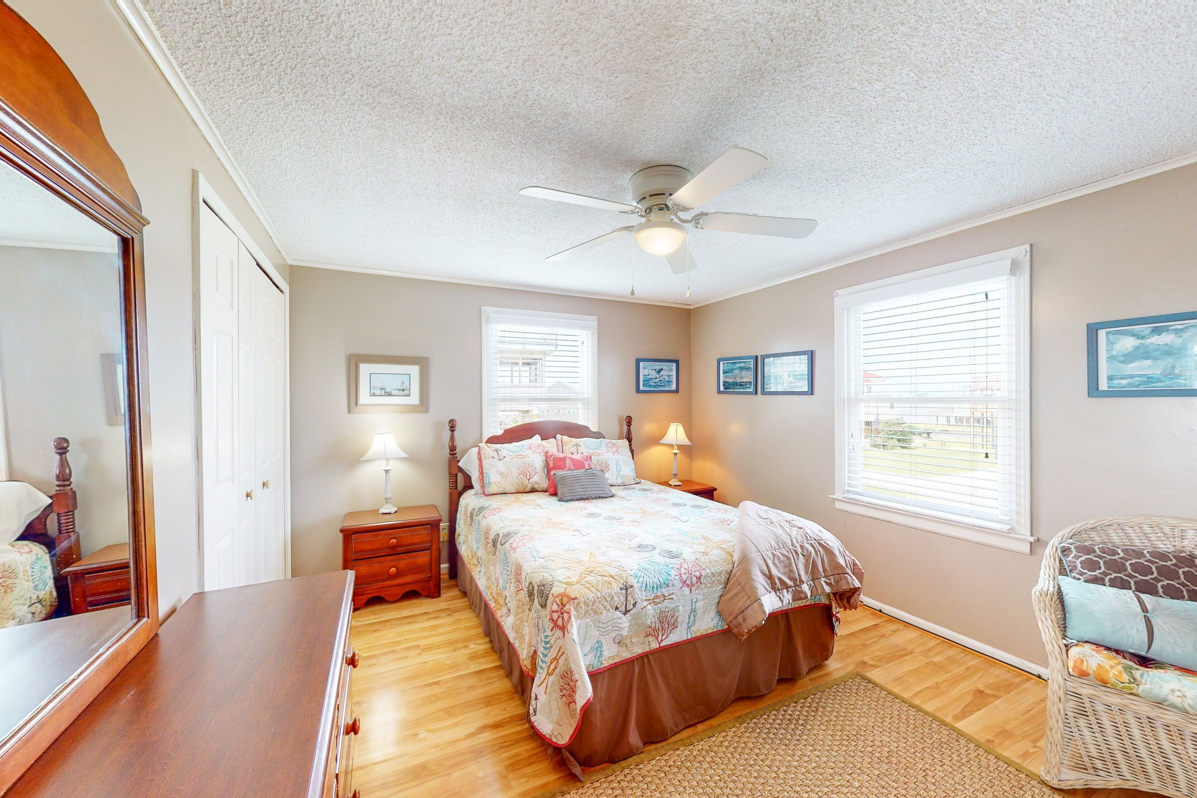 A bedroom with a bed, a ceiling fan, a dresser, a chair, and a window with blinds.