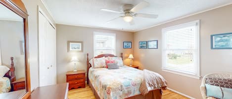 A bedroom with a bed, a ceiling fan, a dresser, a chair, and a window with blinds.