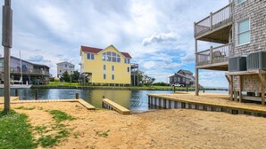 Ein Objekt direkt am Wasser mit Sandstrand, einem Steg und einem gelben Haus mit rotem Dach.
