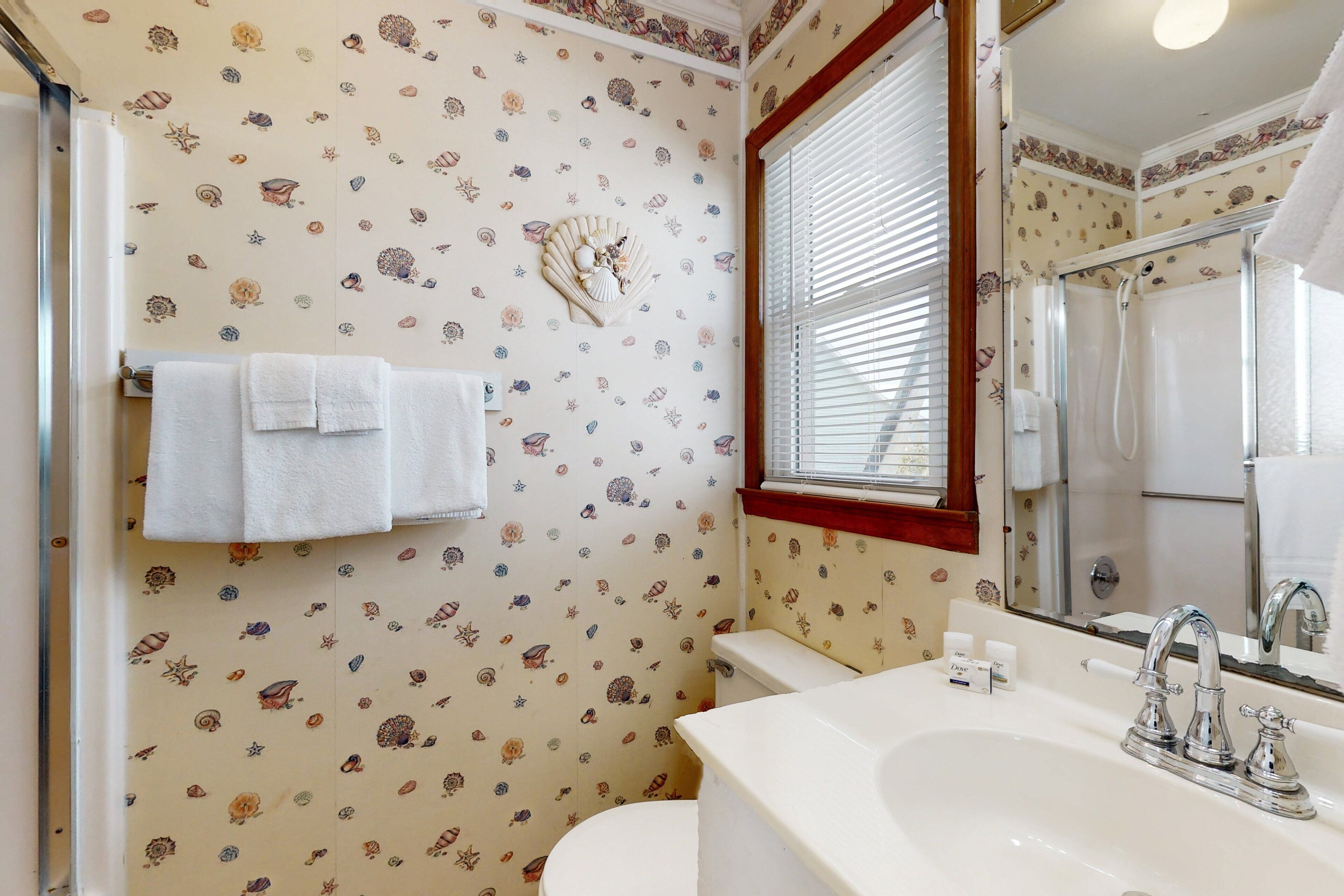 A bathroom with a toilet, sink, and shower. The walls have a seashell pattern.