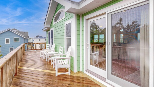 A deck with white chairs, a wooden railing, and a sliding glass door leading to an outdoor area. - Spacious home with private pool, hot tub, pool table & central AC (Waves)