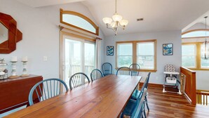 A dining room with a wooden table, blue chairs, a high ceiling, and large windows. - Spacious home with private pool, hot tub, pool table & central AC (Waves)