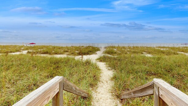 Un sentier de sable qui longe la plage et mène à la mer, avec des garde-corps en bois de chaque côté.