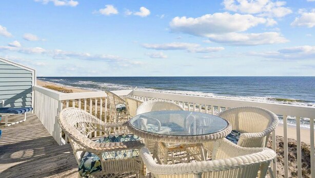 Eine Terrasse direkt am Strand mit Korbmöbeln und einem Glastisch mit Blick auf den Ozean.