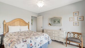 Ein Schlafzimmer mit einem hölzernen Bett, einer weißen Kommode, einem Stuhl und einem Deckenventilator.