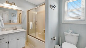 Ein Badezimmer mit einer gläsernen Duschkabine, einem weißen Waschbecken mit Spiegel darüber und einer Toilette mit Fenster.