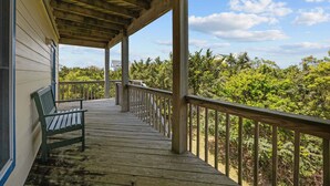 Une terrasse en bois avec un banc, une rambarde et une vue sur une végétation luxuriante.