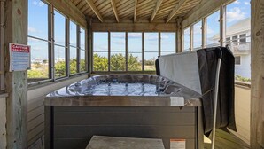 Un bain à remous installé dans une structure en bois dotée de grandes fenêtres, agrémenté d’un panneau d’avertissement et offrant une vue sur la mer.