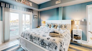 A bedroom with a bed, a nightstand, a lamp, a window with curtains, and a sign above the bed. - Sound front retreat with easy beach access, sauna and private dock for your boat! (Surf City)