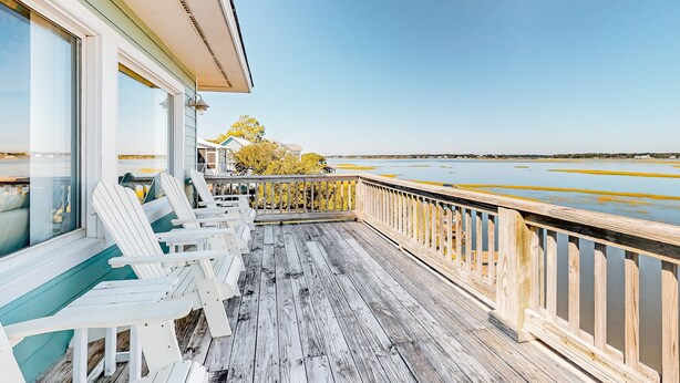 A wooden deck with white chairs and a railing overlooking a body of water. - Sound front retreat with easy beach access, sauna and private dock for your boat! (Surf City)
