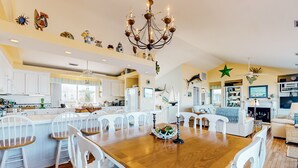 A spacious living area with a wooden dining table, white chairs, and a chandelier. - Sound front retreat with easy beach access, sauna and private dock for your boat! (Surf City)
