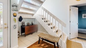 A staircase with white railings leading to a second floor, a wooden bench in the foreground, and a wall-mounted welcome sign. - Sound front retreat with easy beach access, sauna and private dock for your boat! (Surf City)
