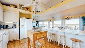 A kitchen with a wooden table, white cabinets, and a large island with stools. - Sound front retreat with easy beach access, sauna and private dock for your boat! (Surf City)