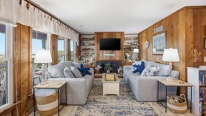 Un salon chaleureux avec deux canapés, un téléviseur à écran plat, des murs en bois et une bibliothèque.