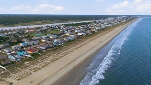 Vue aérienne d’une zone résidentielle côtière, avec des maisons le long de la plage, un ciel dégagé et une mer calme.