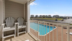 Ein Balkon mit zwei Adirondack-Stühlen, einem Swimmingpool und Blick auf einen Parkplatz sowie Gebäude in der Ferne.